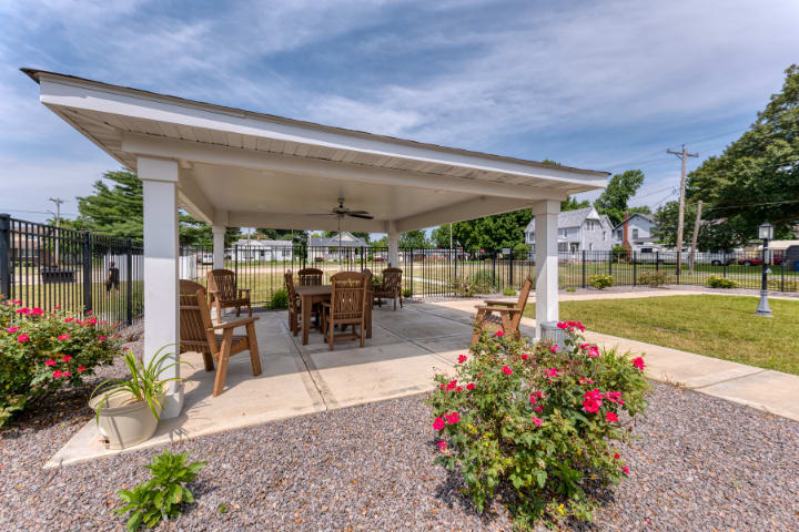 An inviting outdoor gazebo with comfortable seating, surrounded by a landscaped garden and flowers.