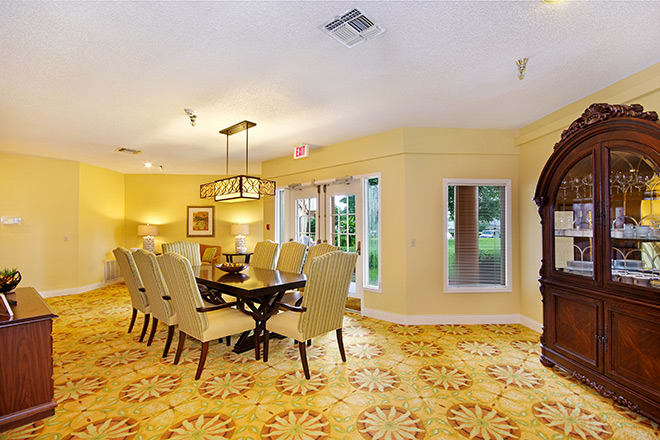 A well-lit dining room with an elegant table and upholstered chairs, featuring stylish lighting fixtures and large windows.