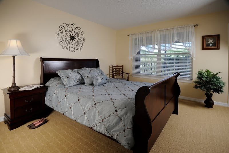 A cozy bedroom with a wooden bed, patterned bedding, and ample natural light.