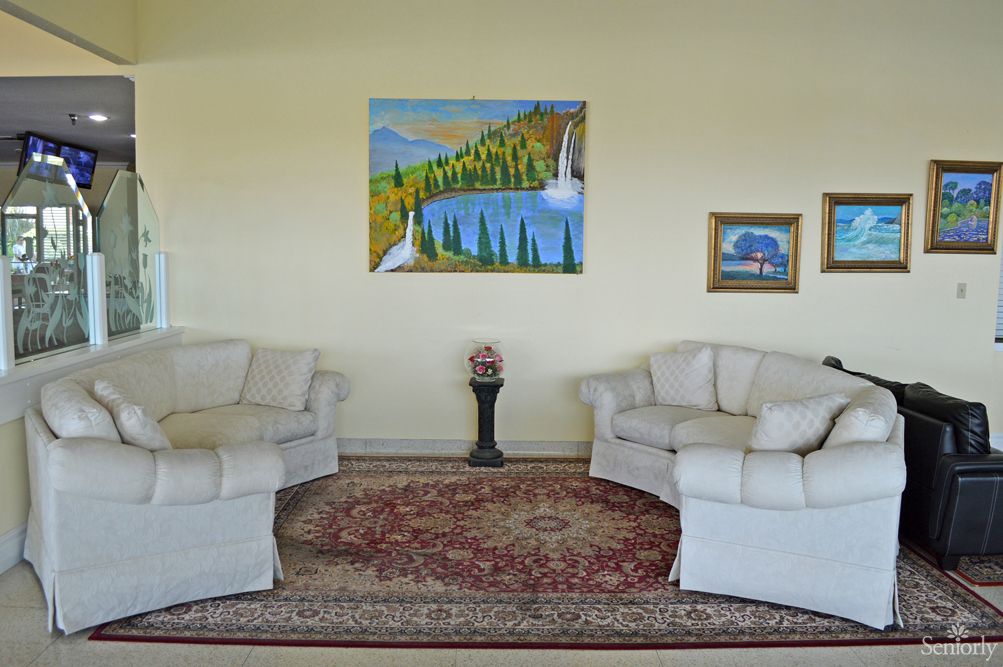 A cozy living room with two white sofas, a patterned rug, and colorful paintings on the wall.