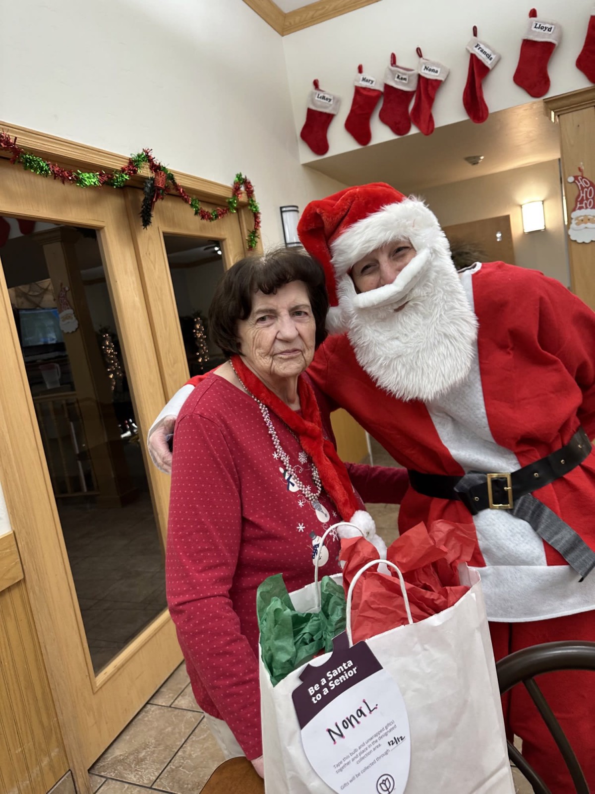 An elderly woman smiling with Santa Claus, enjoying a festive Christmas celebration with gifts.