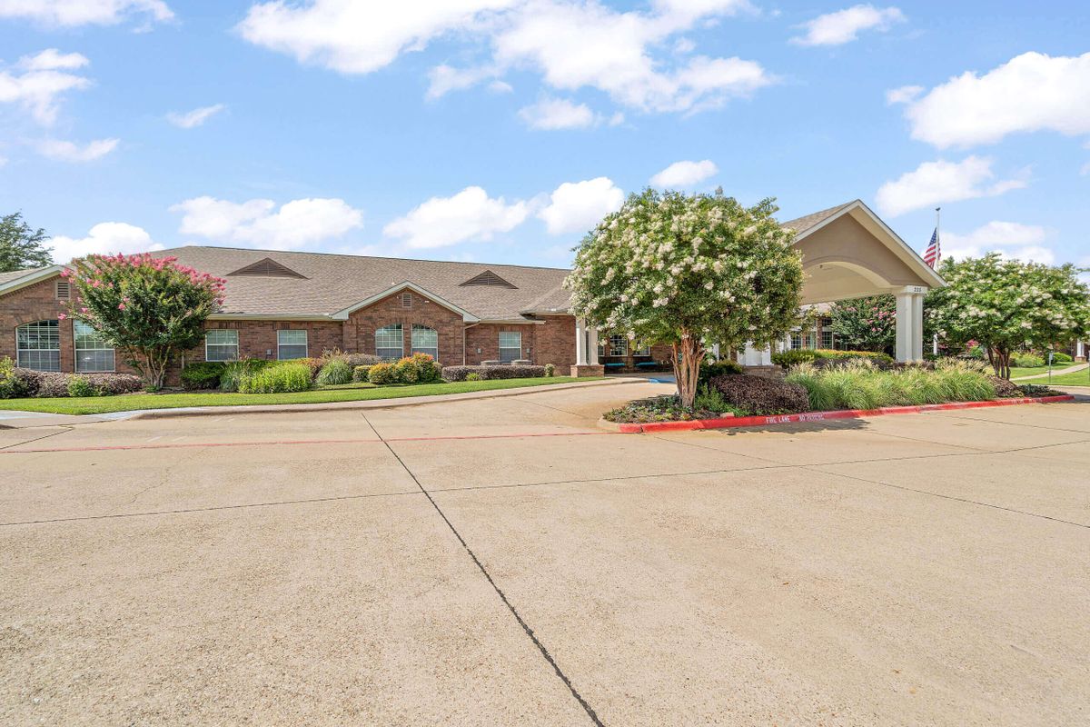 A residential building with a landscaped driveway and a tree under a partly cloudy sky.