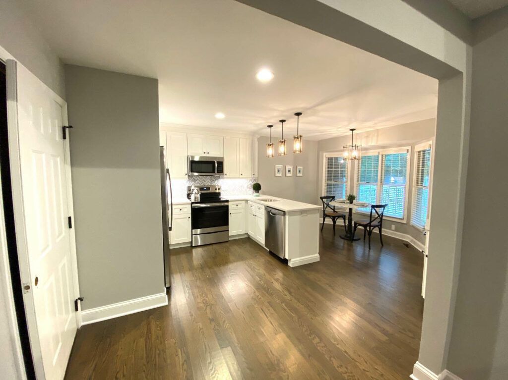 A modern kitchen with an open floor plan, featuring stainless steel appliances, an island, and hardwood floors.