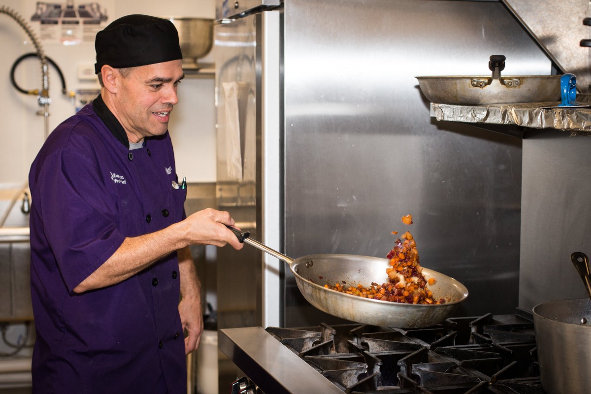 A chef skillfully flips food in a pan while cooking in a professional kitchen.