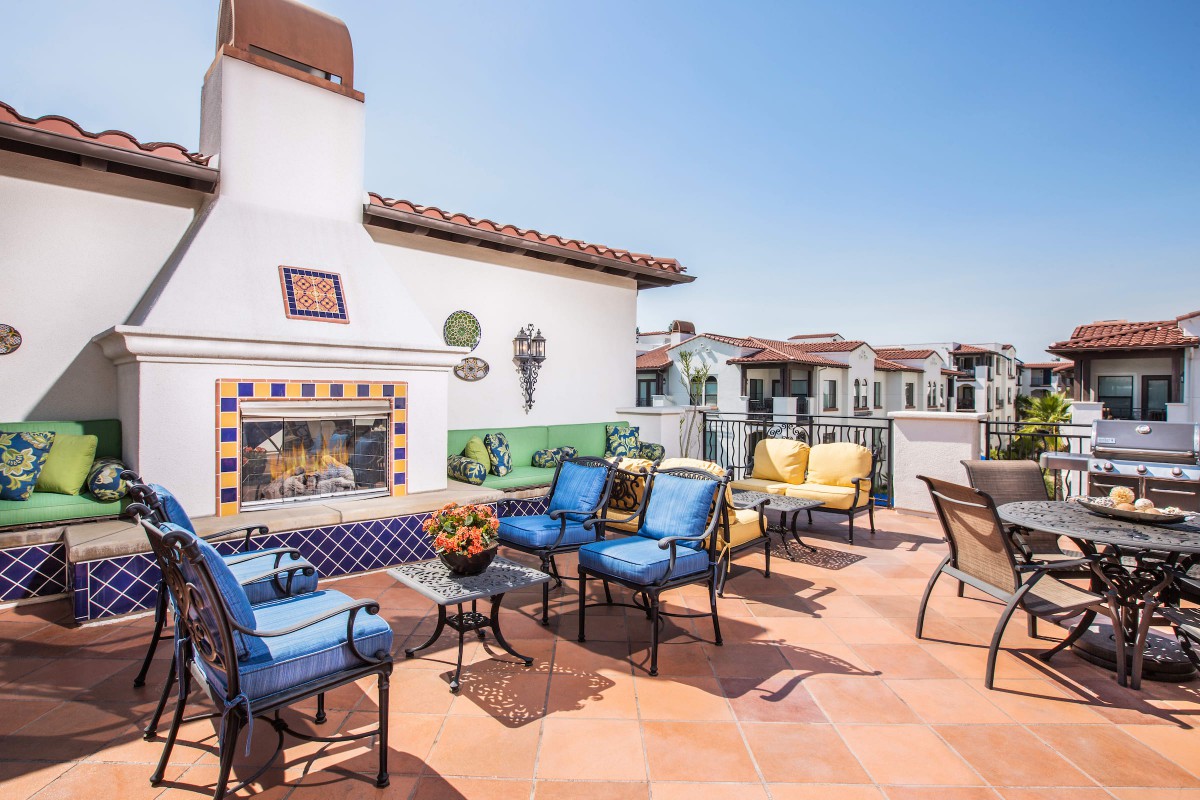 A sunny rooftop terrace with colorful seating and a decorative fireplace.