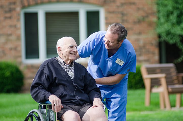 A caregiver spending time with an elderly person in a wheelchair outdoors.