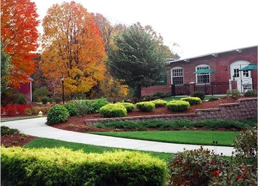 A scenic view of a landscaped garden with vibrant autumn foliage and a pathway leading to a brick building.