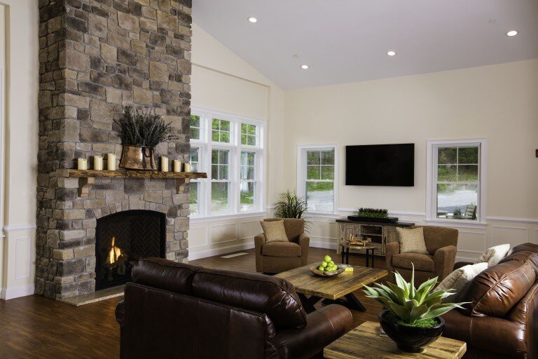 A cozy living room featuring a stone fireplace and leather seating, with a television mounted on the wall.