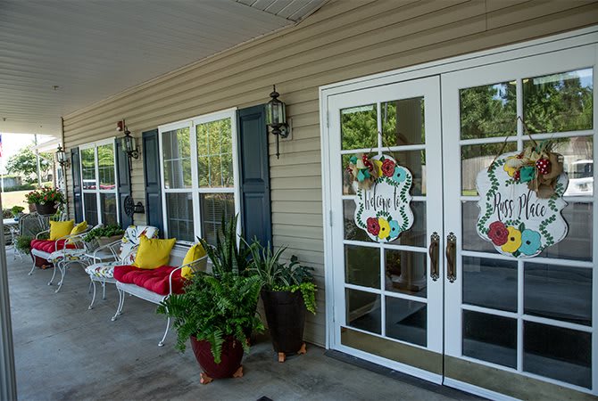 A welcoming front porch with a bench adorned with colorful cushions, potted plants, and decorative glass doors.