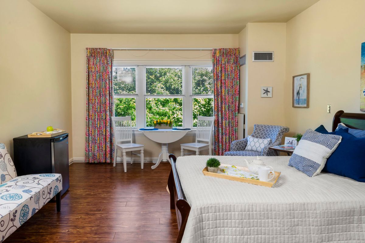 A cozy living room with a seating area by the window, complemented by patterned curtains and wooden flooring.