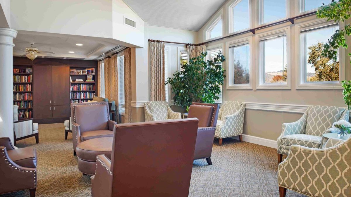 A cozy lounge with comfortable seating and a reading area, illuminated by natural light through large windows.