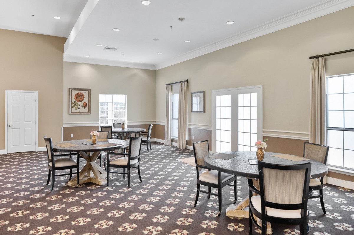 A bright and spacious dining room with tables and chairs, illuminated by natural light from large windows.