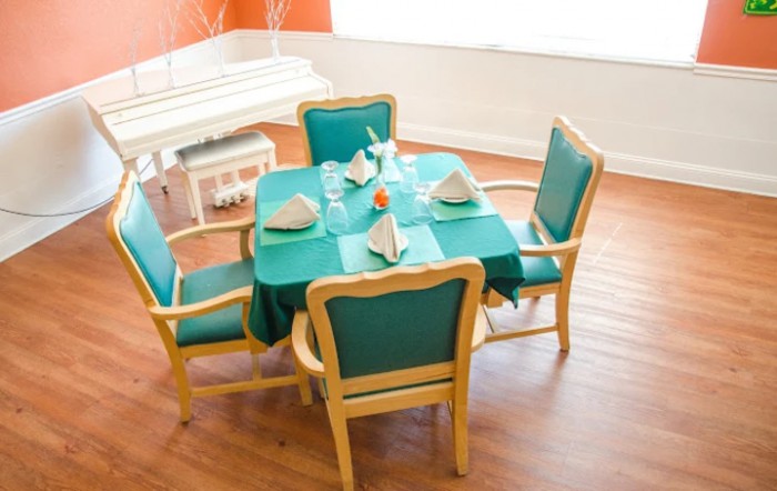 A dining room setup with a square table covered in a teal tablecloth, surrounded by four matching chairs.