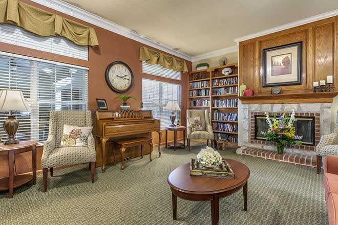 A cozy living room with traditional decor featuring a piano, bookshelves, and a fireplace.