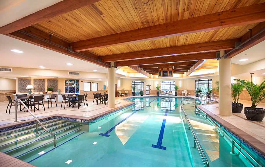 A luxurious indoor swimming pool area featuring wooden ceilings and ample seating.