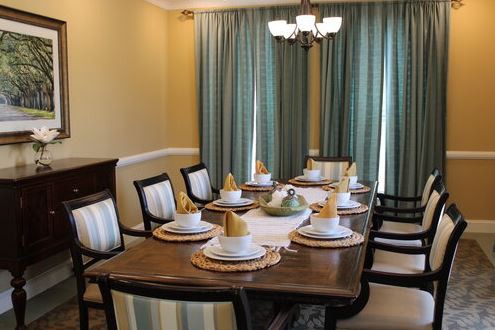 A well-set dining table with elegant place settings and chairs, complemented by teal curtains and a classic chandelier.