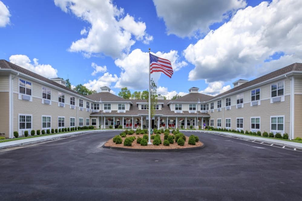 A large building with a circular driveway and an American flag in the center, set against a backdrop of a cloudy sky.