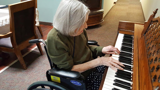 An elderly woman in a wheelchair enjoying playing the piano.