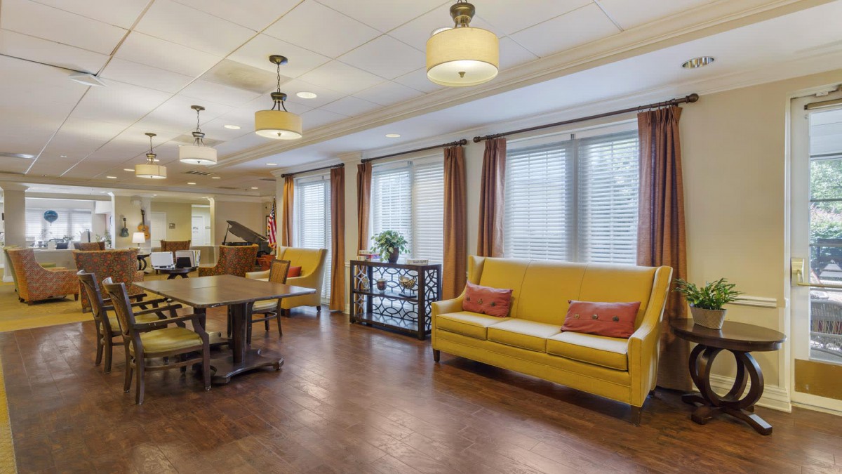 A cozy living room with bright yellow sofas, a piano, and large windows adorned with curtains.