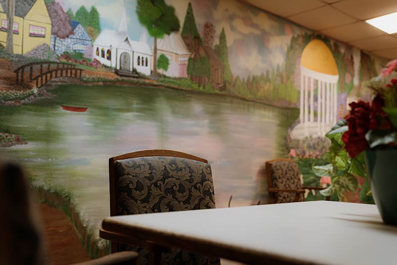 A mural depicting a serene landscape decorates an interior wall, accompanied by chairs and a table.