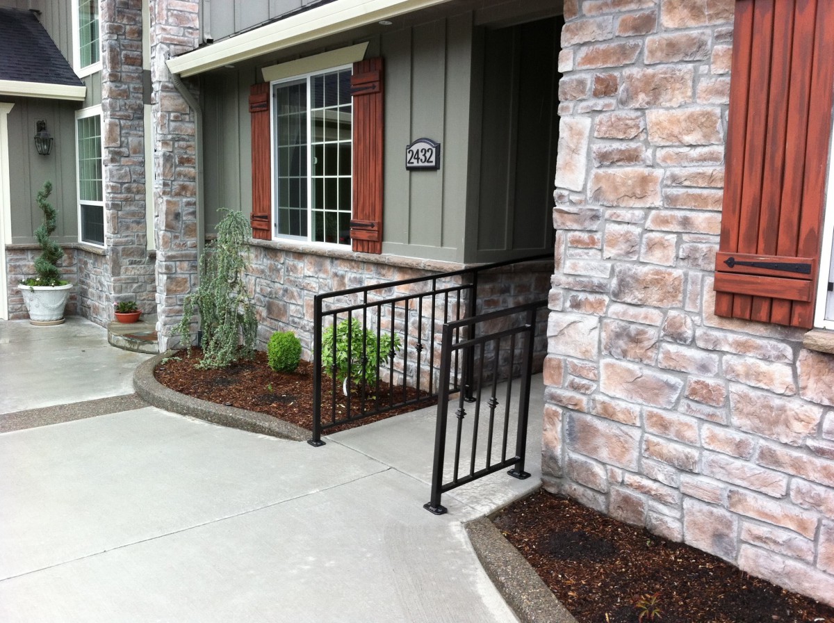 A house entrance with a ramp and railing, featuring a stone facade and landscaped garden.