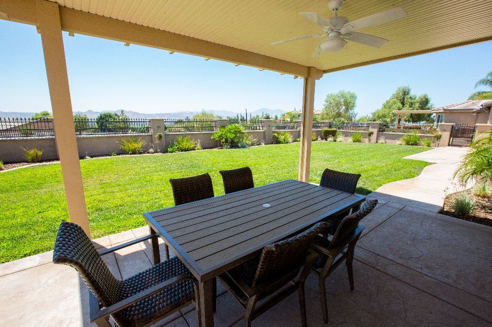 A covered patio with a table and chairs overlooking a green backyard.