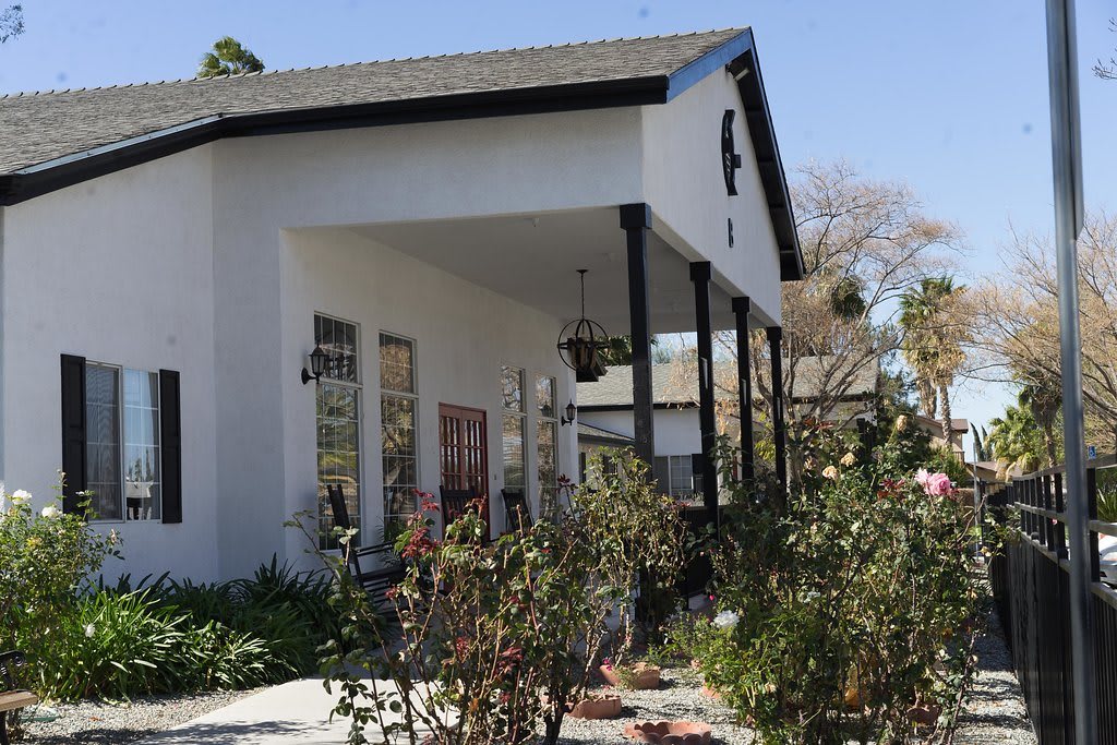 A charming white house with a covered porch and surrounding garden.