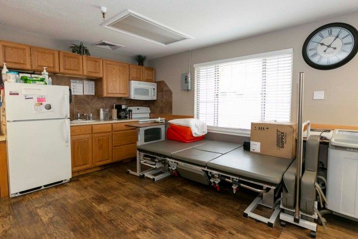 A multi-functional room featuring a kitchen area with appliances and a therapy table by the window.