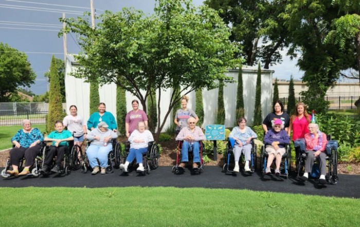A group of people sitting in wheelchairs outdoors in a garden setting.