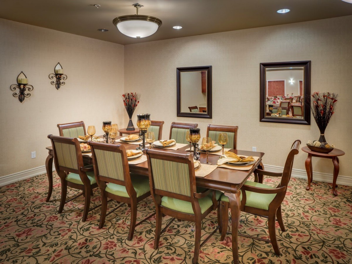 An elegant dining room setup with a large table and chairs, decorated with mirrors and a chandelier.