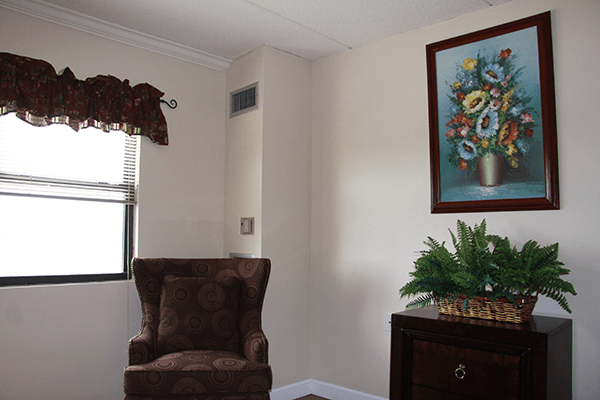 A cozy living room corner featuring an armchair, a vibrant painting, and a potted plant by the window.