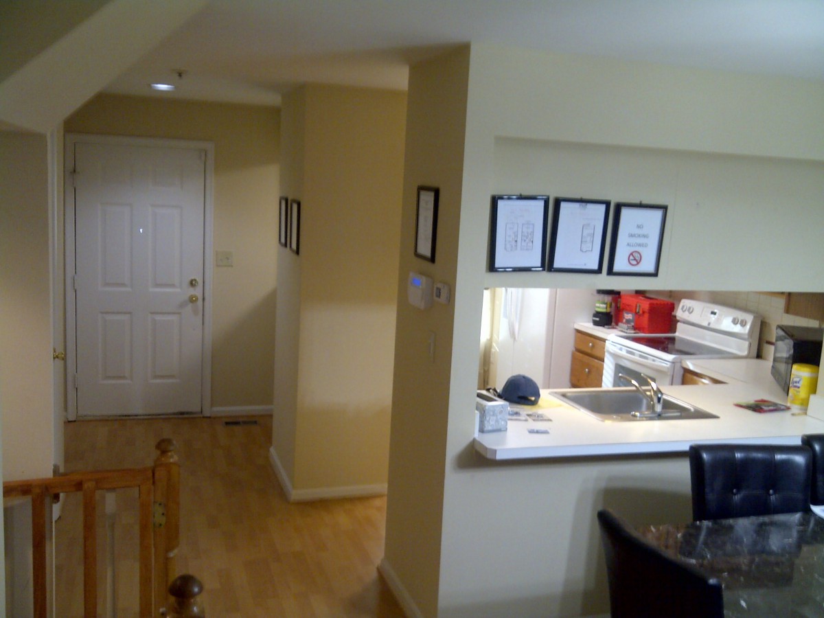 A modern apartment interior featuring a view of the kitchen and adjacent hallway with wooden flooring.