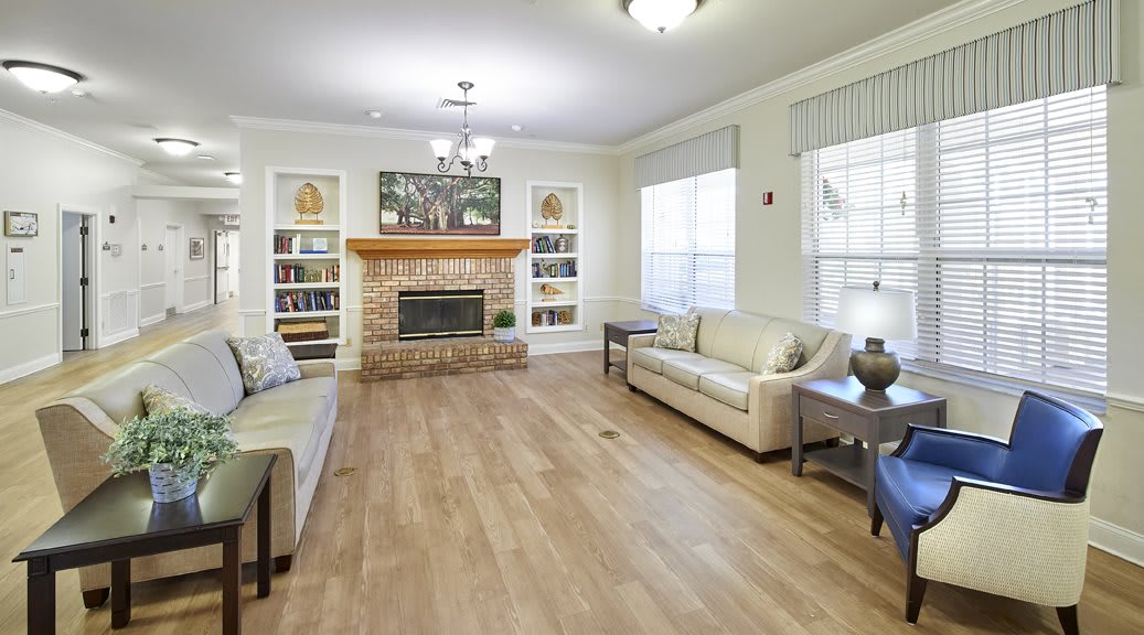 A spacious living room featuring hardwood floors, modern sofas, a central fireplace framed by bookshelves, and large windows.