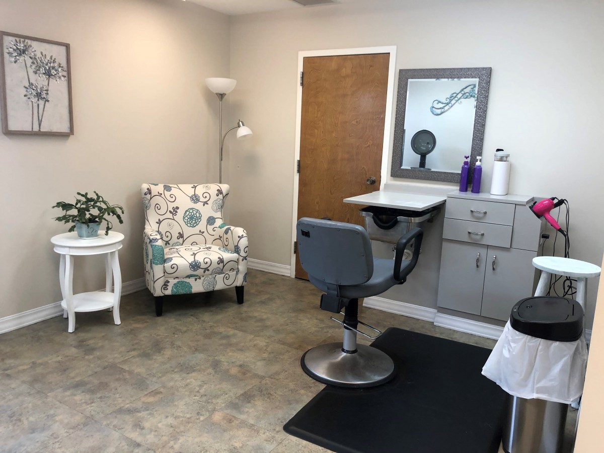 A cozy salon setup with a styling chair, mirror, decorative armchair, and standing lamp.
