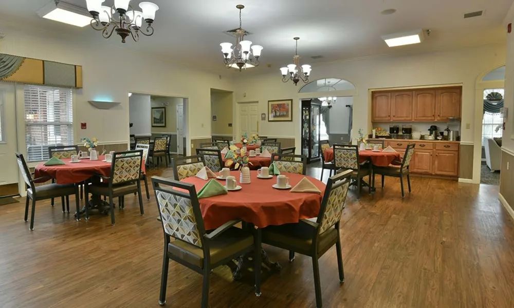 A well-arranged dining room with tables set for a meal, featuring chandeliers and wooden flooring.
