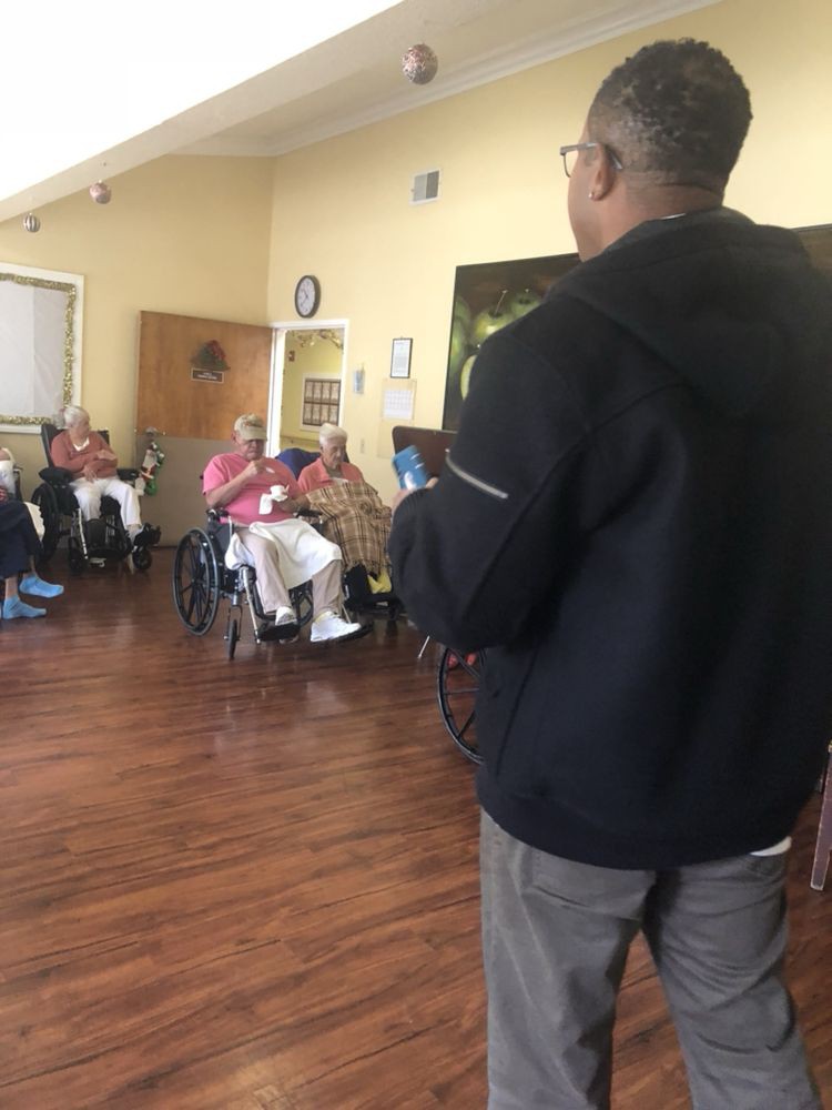 A group of senior citizens seated in wheelchairs, attentively listening to a speaker in a community setting.