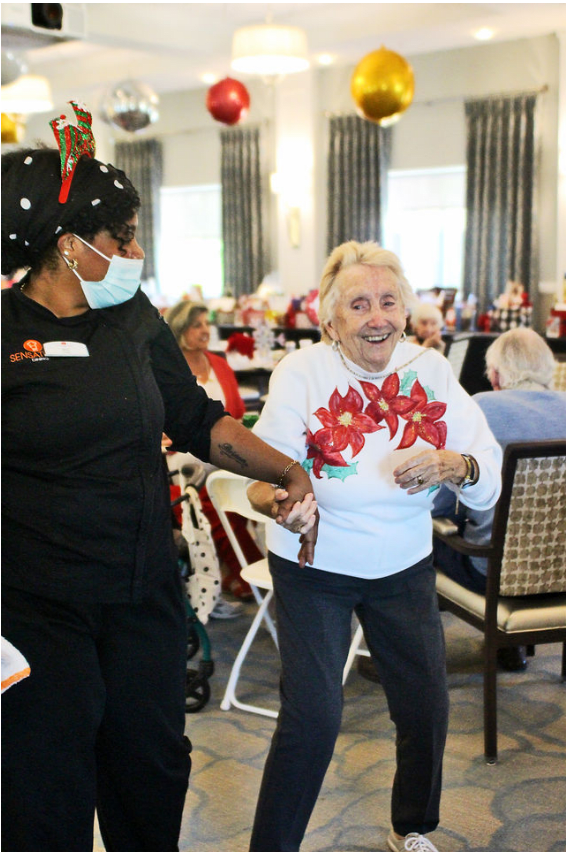 An elderly woman joyfully dances with assistance during a community event.