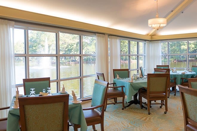 A well-lit dining area with multiple tables and chairs, set near large windows overlooking a scenic view.