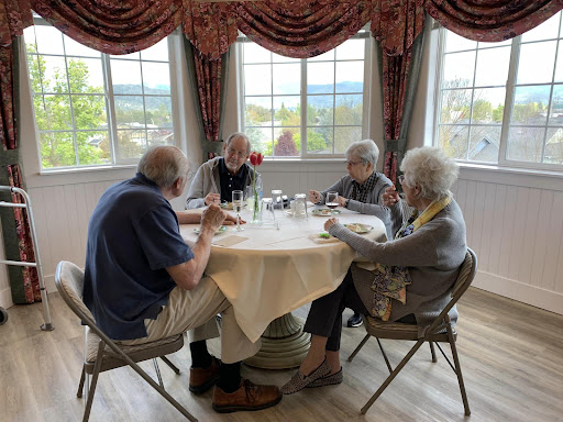 A group of elderly friends enjoying a meal together at a table with a scenic view.