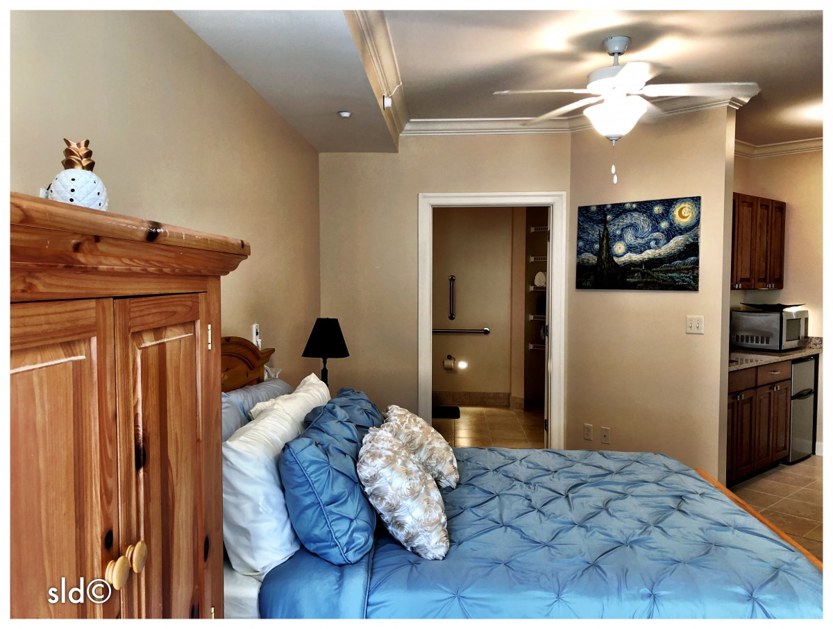 A cozy bedroom featuring blue bedding, a ceiling fan, and a decorative painting.