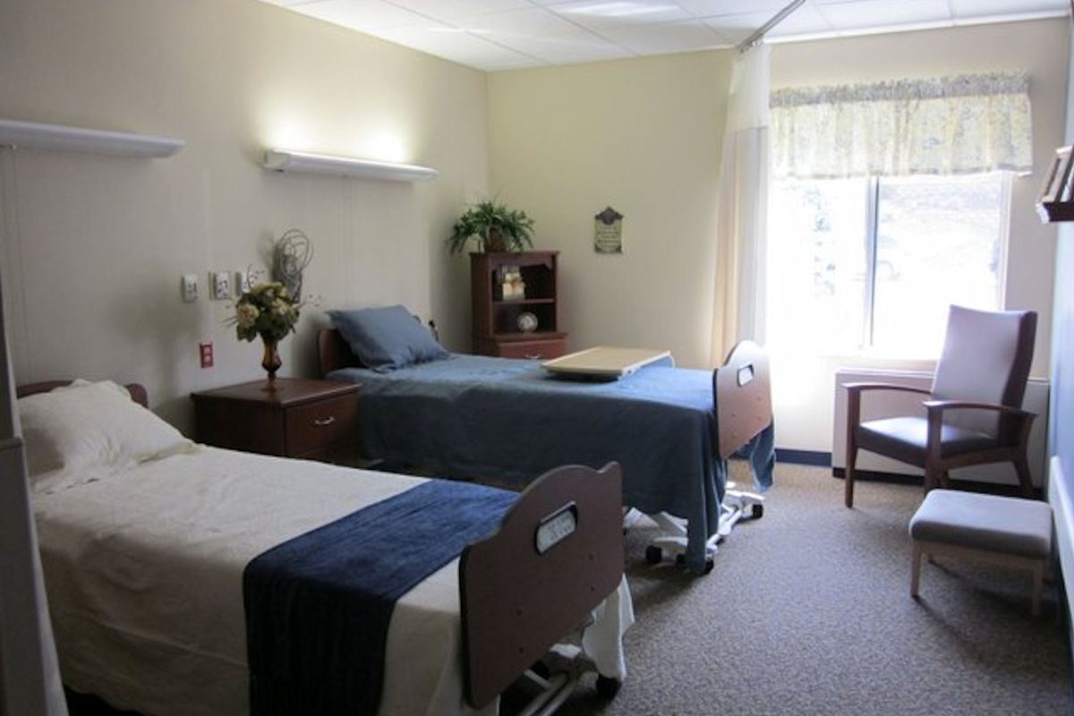 A clean and well-organized hospital room with two beds, a window, and essential furniture.