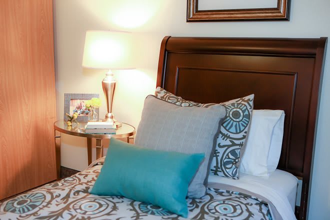 A cozy bedroom setting with patterned pillows, a wooden headboard, and a lit lamp on the nightstand.