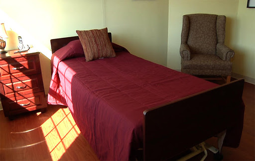 A neatly made single bed with a maroon coverlet and a decorative pillow, accompanied by an armchair in the corner.