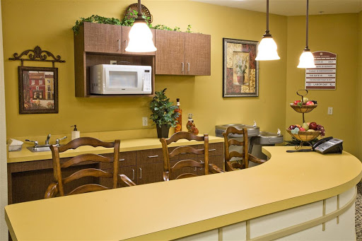 A cozy kitchen featuring warm yellow walls, wooden cabinetry, and a bar area with stools.