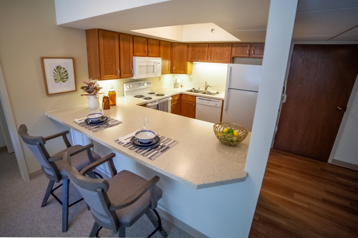 A modern kitchen with wooden cabinets and a clean countertop, featuring stools for seating.