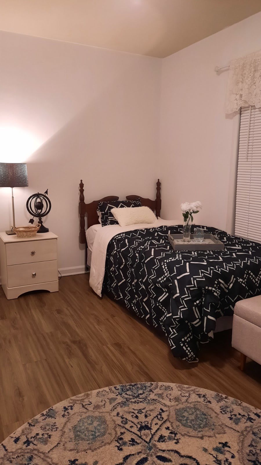 A cozy bedroom with a single bed, patterned bedding, and a nightstand featuring a lamp.
