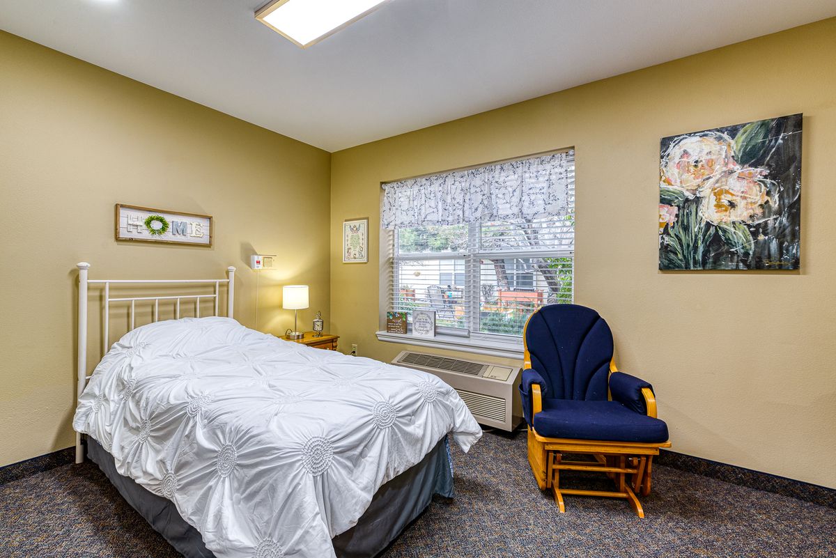 A cozy bedroom with a bed, blue chair, and large window providing natural light.