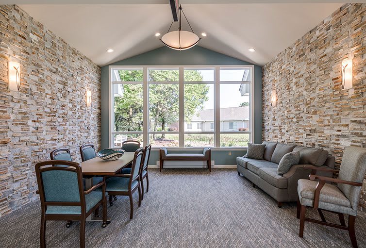 A modern living area with a dining table, couch, large windows, and stone accent walls.