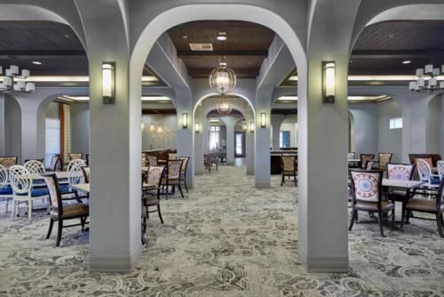 A spacious dining room featuring elegant arches, ambient lighting, and neatly arranged tables and chairs on a patterned carpet.
