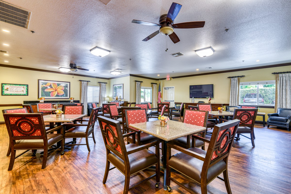 A spacious dining room with multiple tables and chairs, featuring a ceiling fan and bright lighting.
